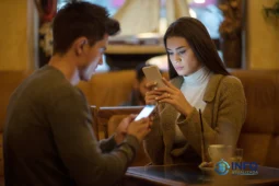 Two people using smartphones in a café while comparing devices and researching options in a smartphone buying guide.